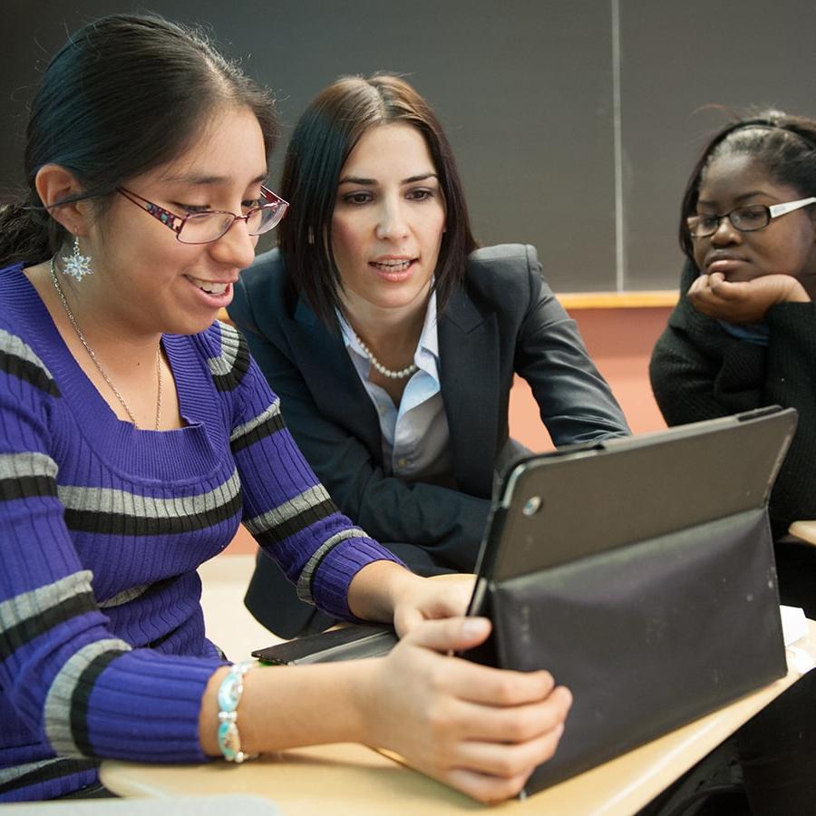 Faculty helps student on laptop in a classroom.